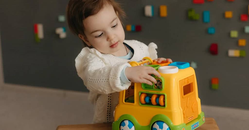 A young child playing with a colorful toy truck indoors, showcasing creativity and curiosity.