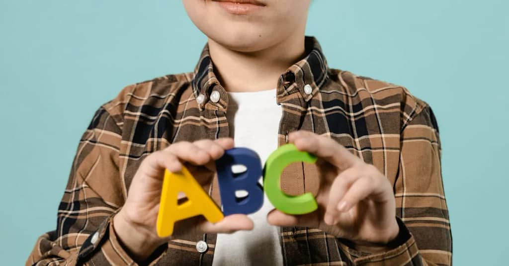 Young boy holding vibrant ABC letters on a blue backdrop, symbolizing childhood learning.