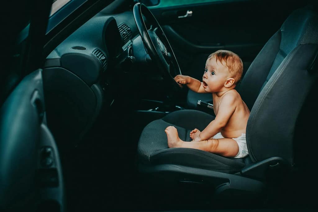 Cute baby sitting on the driver's seat of a car, looking curious and playful.