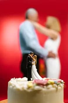 Wedding cake with romantic toppers, blurred couple in warm embrace, celebrating an anniversary indoors.