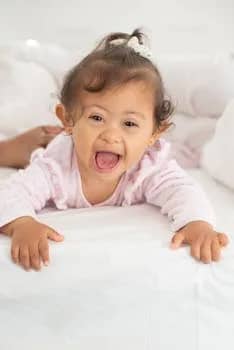 Adorable baby girl with Down syndrome happily lying on a bed indoors.