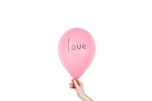 A hand holding a pink balloon with 'love' written on it, against a white background.