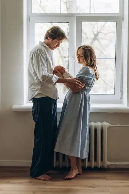 New parents lovingly hold their newborn by a bright window, epitomizing family affection.