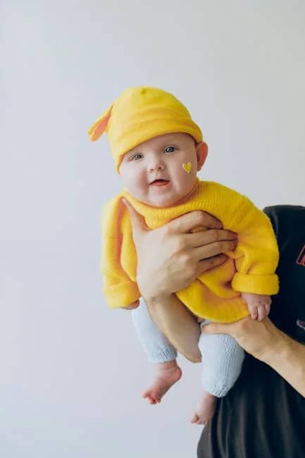 Cute baby in a yellow outfit being held indoors against a light background.