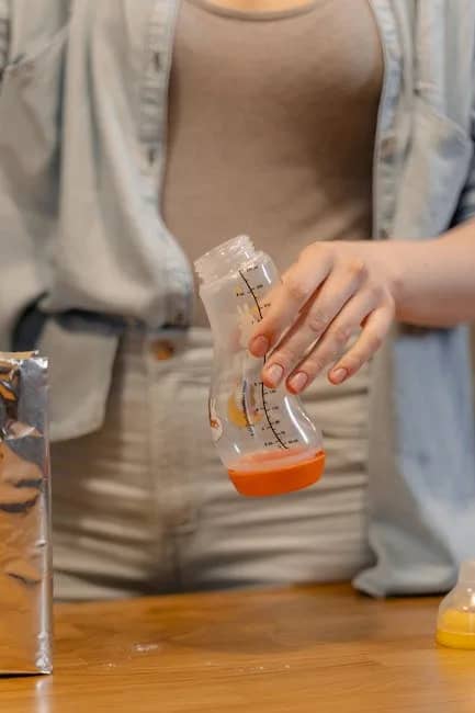 A person preparing a baby bottle with infant formula indoors in a casual setting.