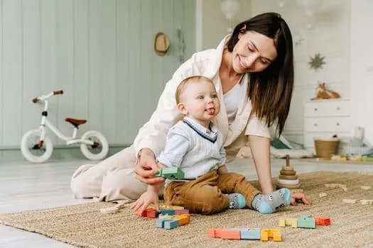 A joyful scene of a mother playing with her baby boy on the floor with colorful wooden blocks.