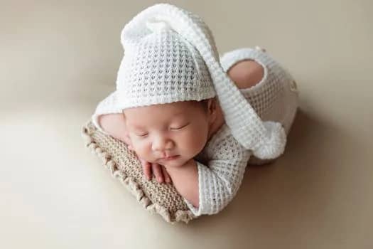 A serene image of a newborn baby wearing a knit outfit with a long hat, sleeping peacefully indoors.