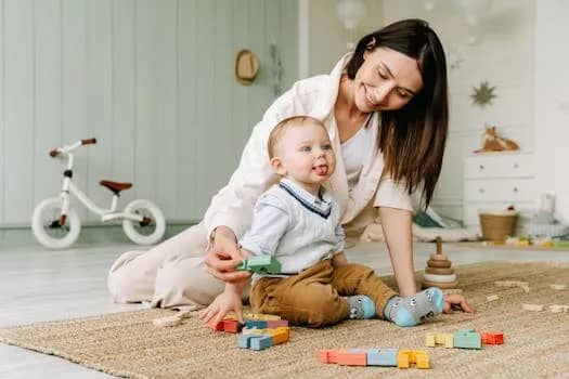 A joyful scene of a mother playing with her baby boy on the floor with colorful wooden blocks.