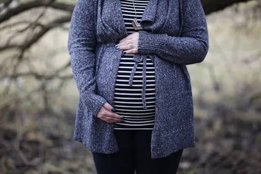 Pregnant woman in striped shirt and cozy sweater outdoors, embracing motherhood.