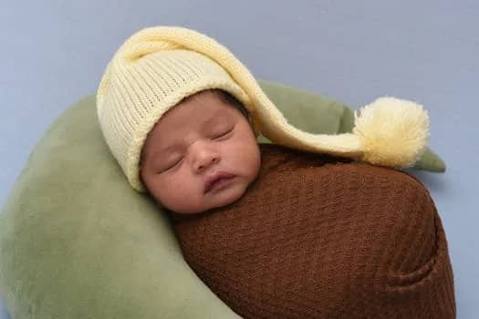 Close-up of a newborn baby peacefully sleeping in a cozy brown wrap and yellow knit hat.