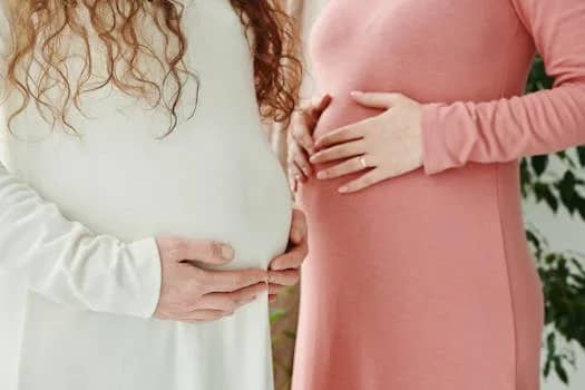 Two expectant women gently holding their pregnant bellies, symbolizing motherhood and maternity.