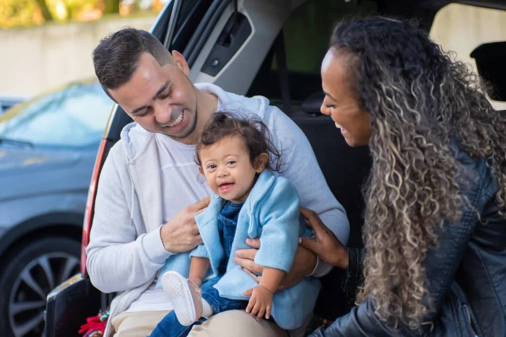 A joyful family moment captured inside a car trunk with parents and their toddler laughing.