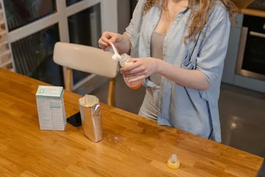 A woman prepares baby formula in a modern kitchen, captured during a daytime routine.