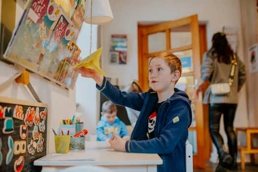 A young boy enjoying a creative activity with a paper airplane in a lively classroom setting.