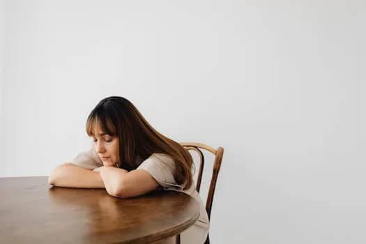 A calm and serene portrait of a woman resting with eyes closed at a wooden table.