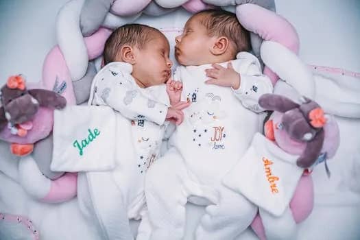 Cute twin babies peacefully sleeping with plush toys, wearing matching pajamas indoors.